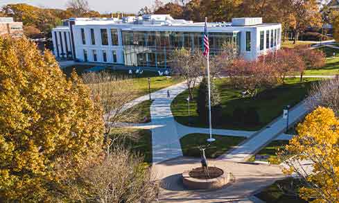 Campus view featuring lush trees and a flag, creating a serene and inviting atmosphere.