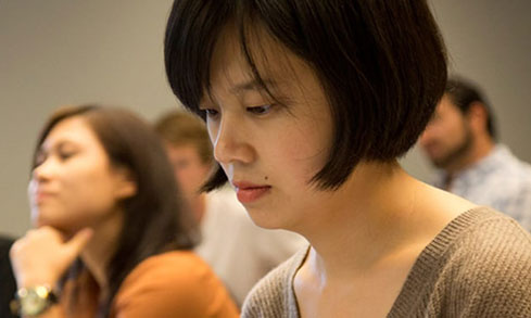 A woman sits in a classroom surrounded by classmates, engaged in a learning environment.