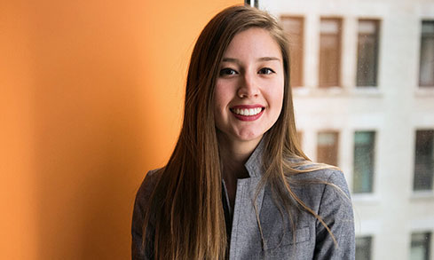 A young woman in a business suit smiles confidently.