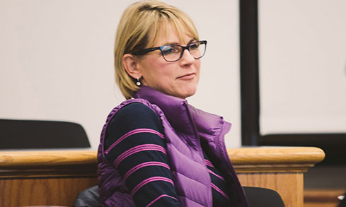 A woman wearing glasses sits attentively in a classroom.