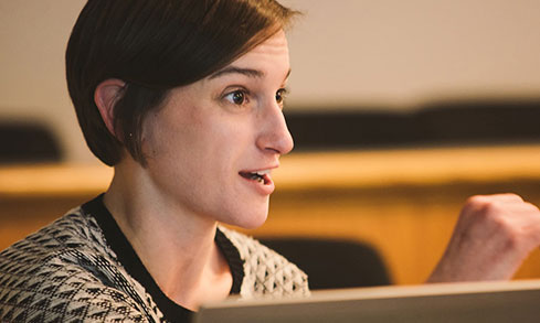 A woman sits in a classroom with a thoughtful expression on her face.