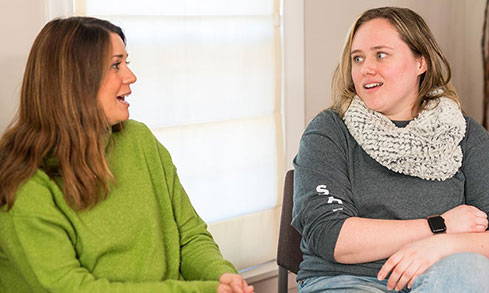 Two women sitting in a chair, engaged in a friendly conversation.