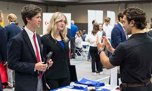 A diverse group of individuals gathered around a table, engaging in conversation with a man and woman at the center.