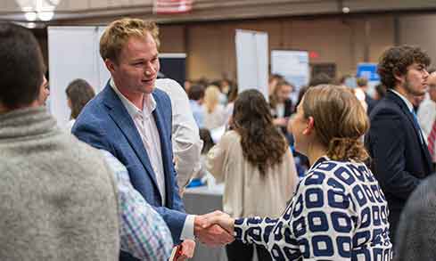 A man and a woman shake hands at a job fair, symbolizing a professional connection and networking opportunity.