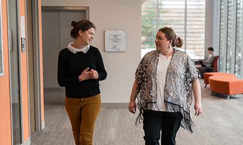 Two professors walk down a hallway talking to each other.