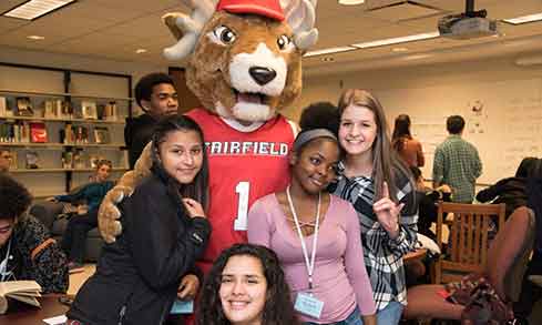 students pose with a stag mascot in a classroom.