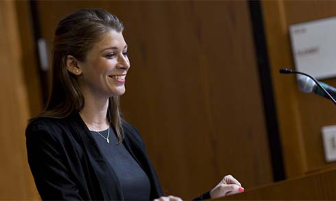 Student smiles at podium in front of wooden walls. 