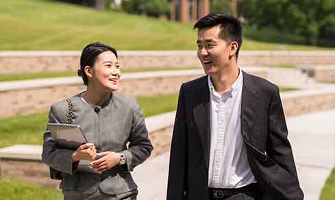 Two business professionals walking together on a grassy area, engaged in conversation and collaboration.