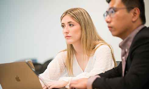 Two individuals engaged in work at a table, each using their laptops for collaboration or productivity.