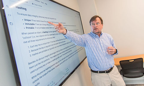 Professor giving a presentation and pointing to a screen that says “Hashing” on it.