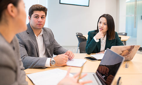 Three business people engaged in discussion at a table in a meeting room.