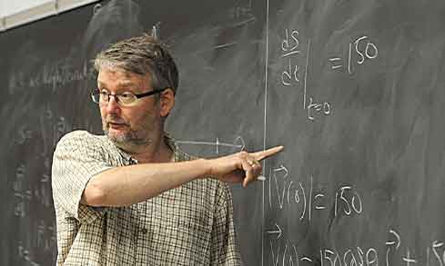 A professor points to math on a chalkboard.