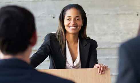 A woman in a black suit smiles at two people at the other side of a table.A 