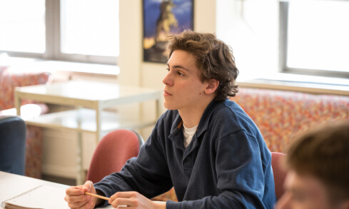 A student sits at a desk holding a pencil.