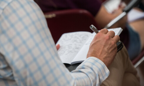 A student writes in a journal propped up on their lap.