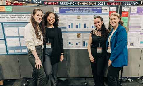 A group of students stands in front of their research poster that is titled “The Impact of Adolescent Social Isolation on Depressive-like Behavior and Alcohol Preference in Male Rats”.