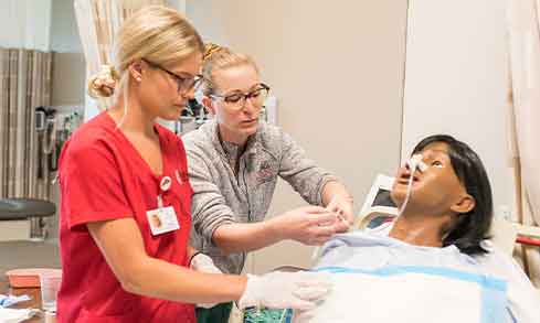 A nurse caring for a simulation patient in a hospital room.