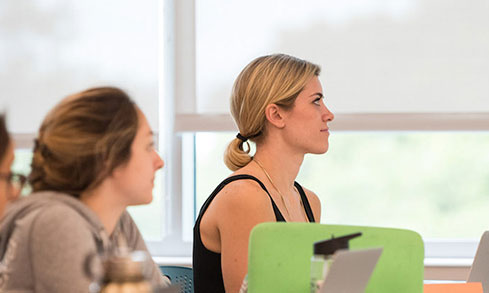 A diverse group of students sits at a table, engaged with their laptops and sharing ideas.