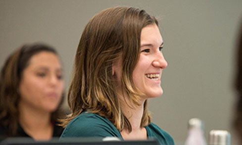 A woman smiles happily in class surrounded by friends, enjoying a joyful moment together.