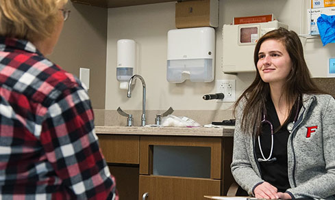 A nursing student sits with a patient in a doctor's office.