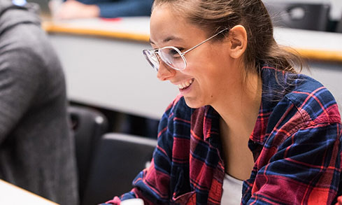 Students in classroom smile at laptops.