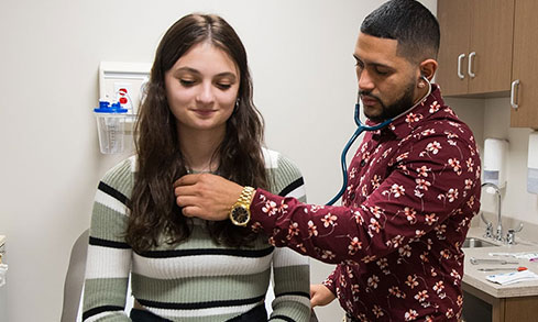 Two nursing students in a doctors office practice using stethoscopes 