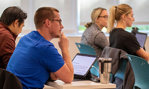 Students in a lecture look up from laptops and listen to professor