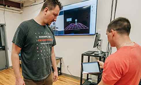 Two students model an engineering design for a professor.