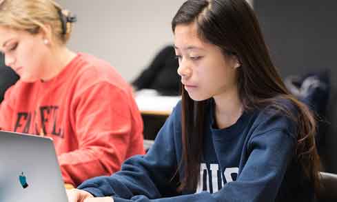 A student sits at a desk using a laptop.