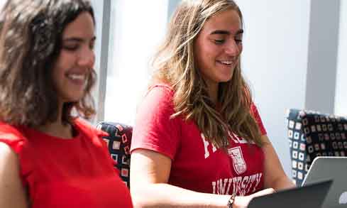 Two students in red shirts work on a laptop.