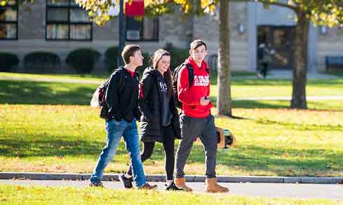 Three students walking on a path with backpacks.