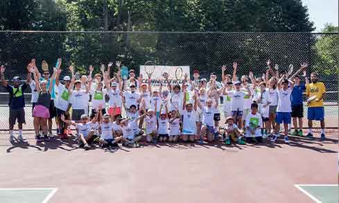 A large group of tennis camp students pose for a photo with instructors.