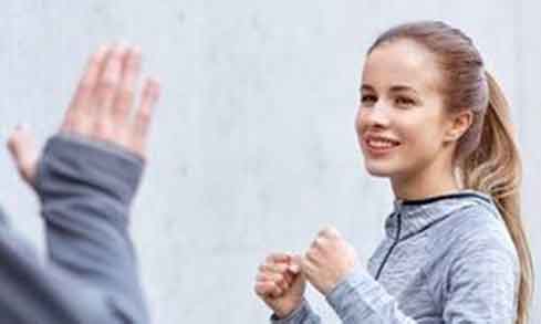 A woman holds her hands up in defense against another person.