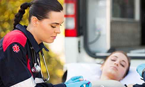 Two EMTs at work in front of a patient laying on a gurney.