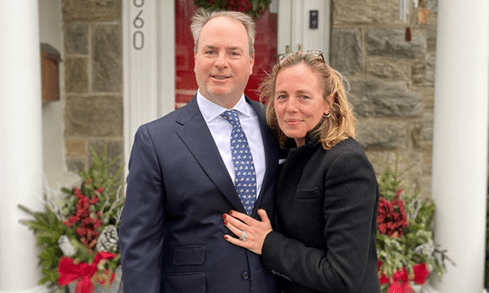 Two people smile for a photo in front of a front door.