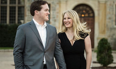 Two people smile in front of a stone building.