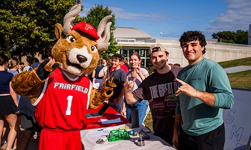 Students smiling and posing with the "Stags Up" hand sign with the Fairfield mascot, Lucas the Stag.