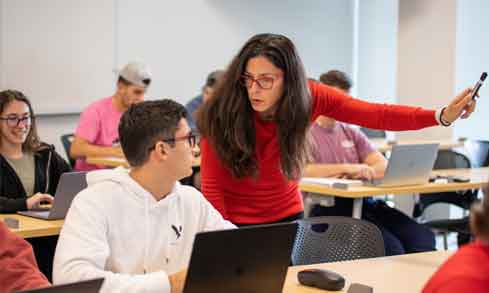 Professor standing next to seated student discussing the subject matter in a classroom.