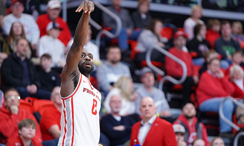 A male basketball player in a red jersey has his arm raised from shooting a ball.