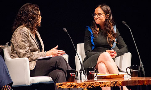 Two women sitting on chairs, engaged in a friendly conversation with smiles on their faces.