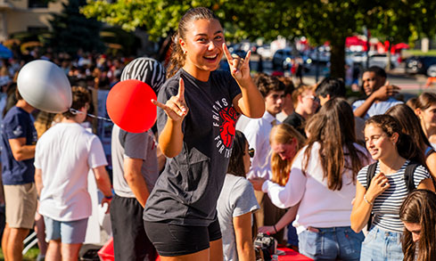 A woman in a black shirt stands with red and white balloons, looking cheerful and vibrant.