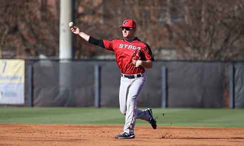 Baseball player in a red jersey that reads “Stags” throws a baseball.