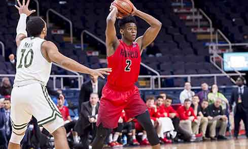 Basketball player in a red jersey that reads “Fairfield 2” holds a basketball above his head.