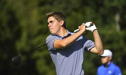 A student in a blue striped polo finishes a golf swing. 