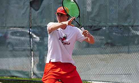 A tennis player in a white Fairfield t-shirt holds a tennis racket. 