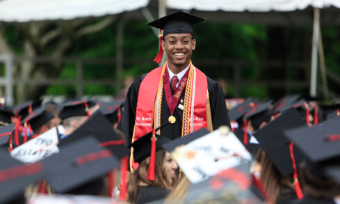 A graduate in cap and gown attire stands in a crowd.