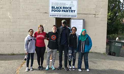 A group of students smile in front of a sign that reads “Black Rock Food Pantry”.