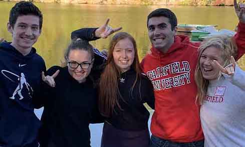 A group of students hold up their hands in a stag shape in front of a lake.