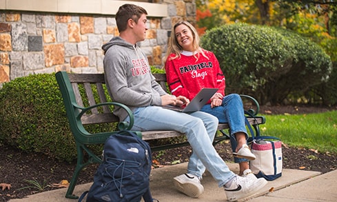 Two students sit on a bench outdoors.