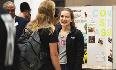 Two people engaged in conversation in front of a poster board displaying information.